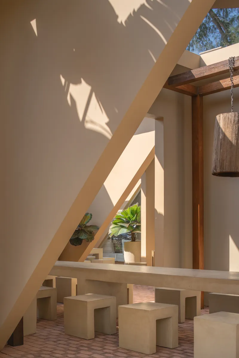 Angular wall casting shadow over a raised dining platform with benches beneath a skylight and timber beams