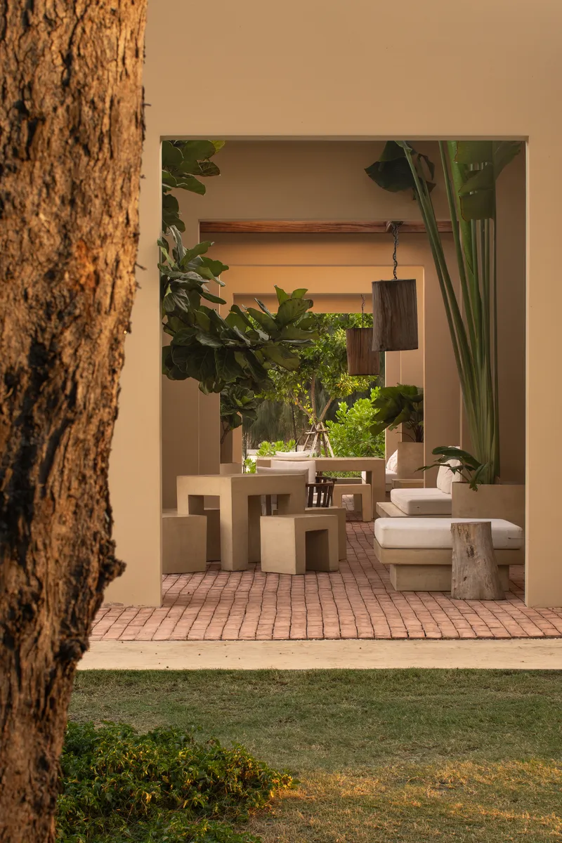 View through the entry opening to a brick-paved terrace with sculptural furniture and potted plants
