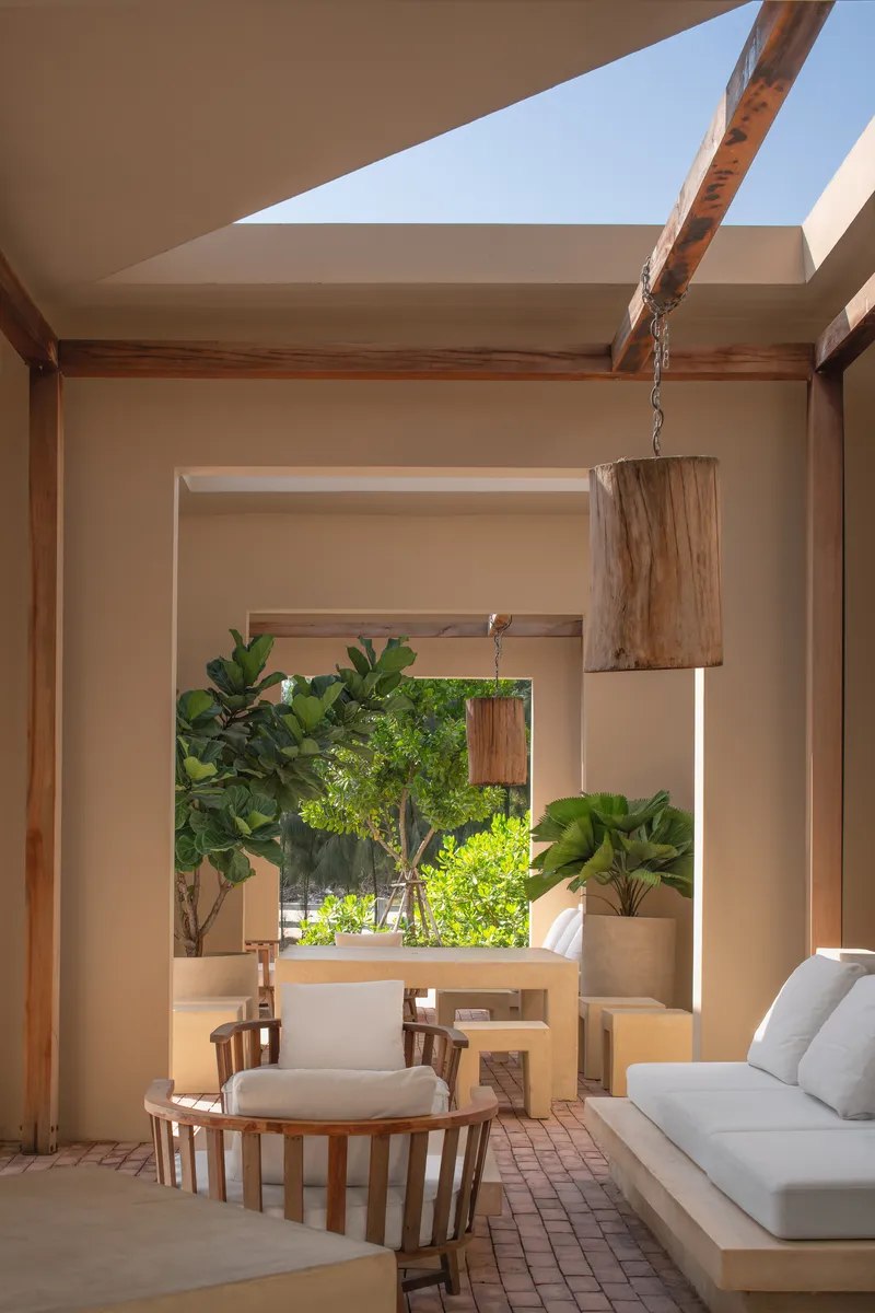Framed view through sequential openings to a planted courtyard with suspended timber light fixture