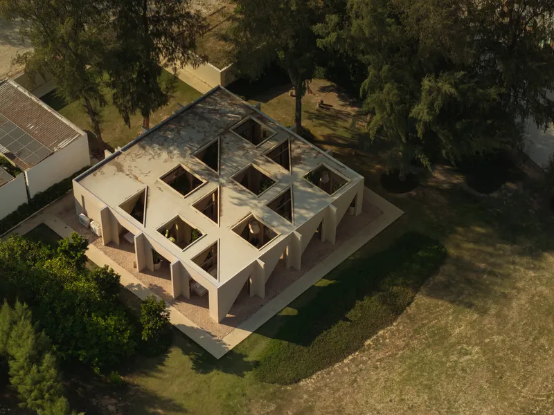 Aerial view of a square pavilion with sawtooth roof vaults arranged around interior courtyards in a grove