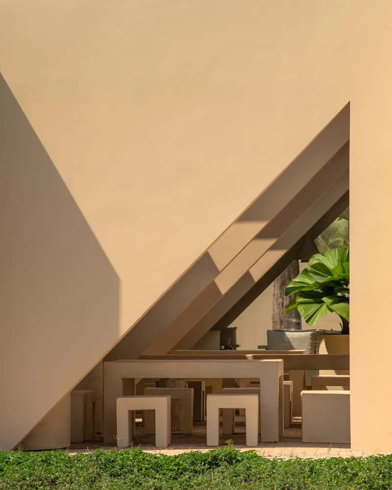 Courtyard view of stacked beige stucco frames beneath an angled roof with palm trees visible beyond