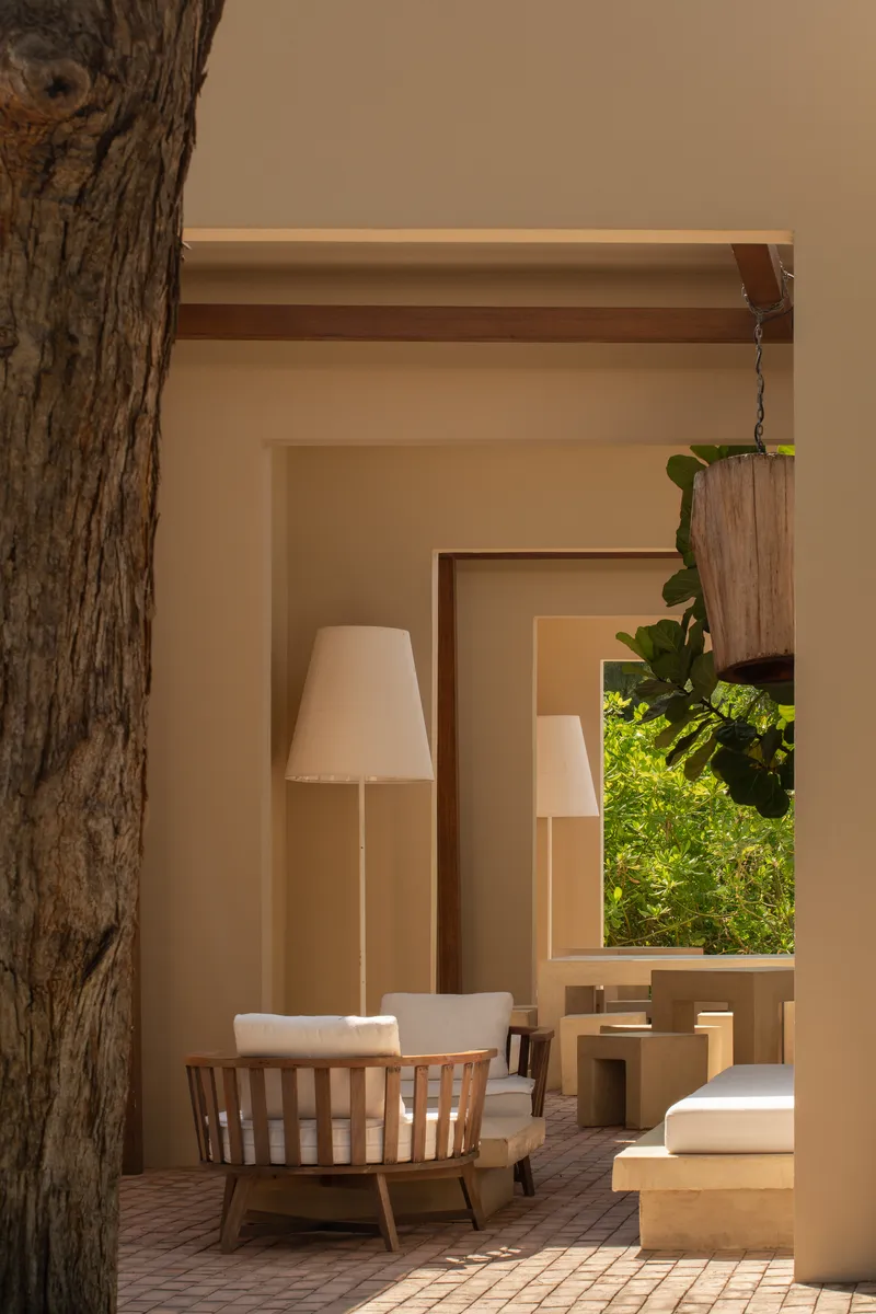 Covered terrace with brick paving, wooden chair and floor lamps framed by a tree trunk