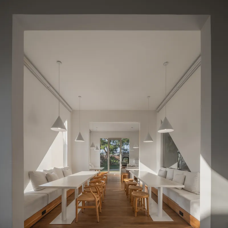 White dining room with built-in benches, timber chairs and pendant lights casting triangular shadows