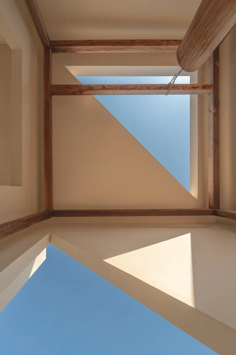 Upward view of skylight framed by timber beams showing blue sky and diagonal shadows