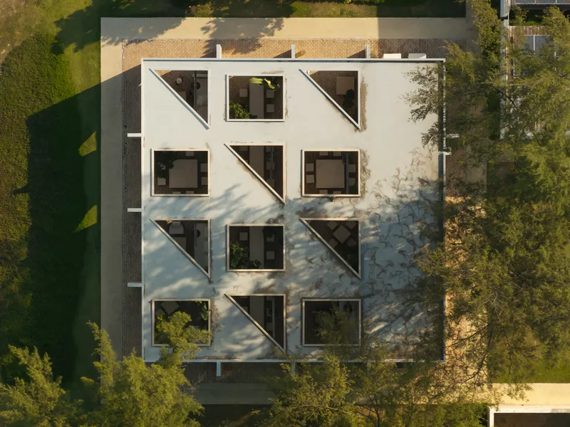Aerial view of white facade with diagonal window awnings and tree shadows in afternoon light