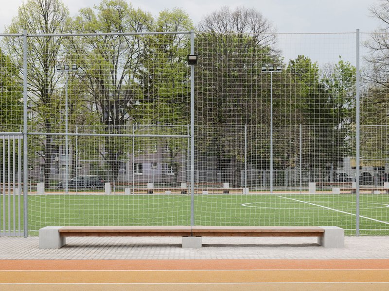 Timber bench with concrete endcaps facing a synthetic turf sports pitch enclosed by wire fencing