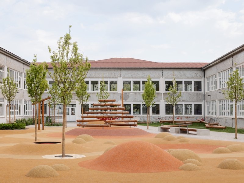 Courtyard with timber climbing structure, young trees and sculpted sand mounds in coral and ochre tones