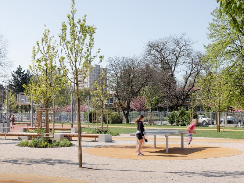 Outdoor play area with planted beds and young trees as two runners pass through