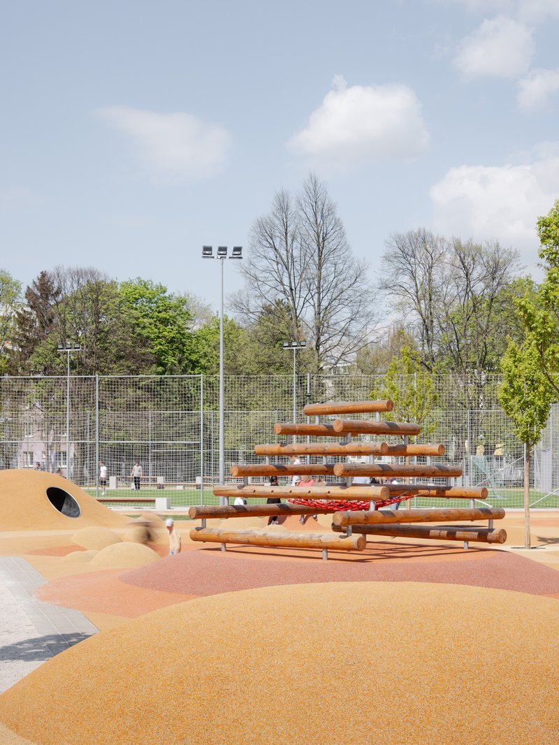 Timber climbing structure on an orange rubber surface with sports field visible behind