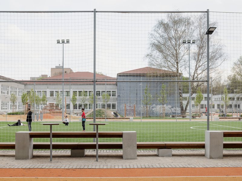 Concrete and timber benches at courtside with children playing on the sports field beyond