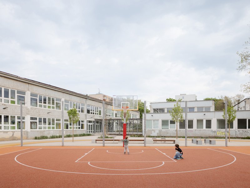 Basketball court with orange rubber surface where two children play beneath a cloudy sky
