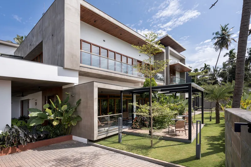 Garden view of the stacked concrete and white volumes with steel-framed pergola surrounded by palm trees