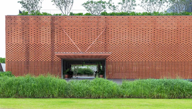 Perforated brick facade with chevron pattern above a central passage, fronted by planted beds and lawn
