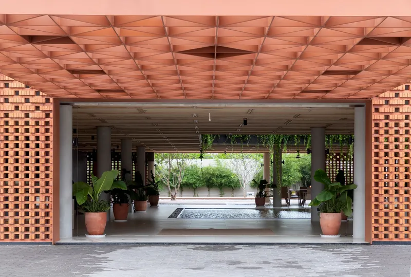 Covered entry passage with geometric timber ceiling and open brick screens flanking potted plants