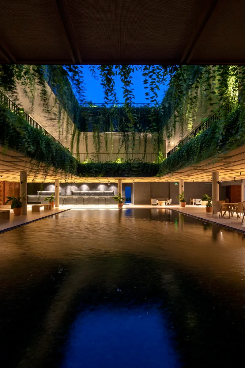 Open courtyard pool with cascading green walls rising toward a blue twilight sky