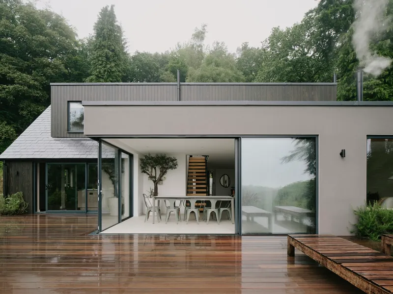 Open glass doors connecting the dining area to a wet timber deck under misty skies