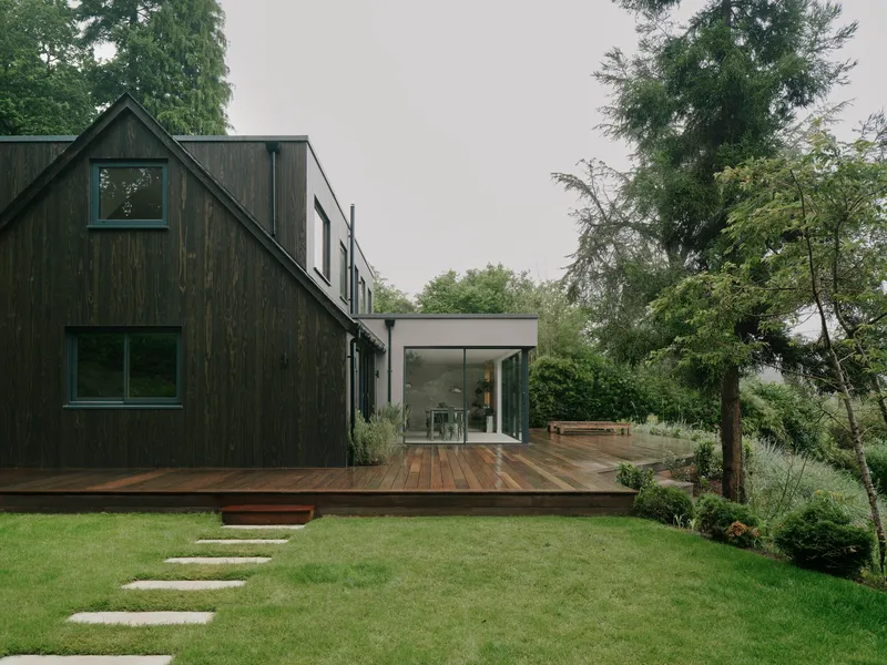 Blackened timber gable volume and glazed extension overlooking a stepped stone path through lawn