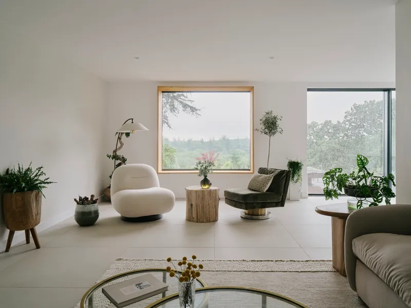 Living room with timber-framed window and corner glazing framing misty green landscape views