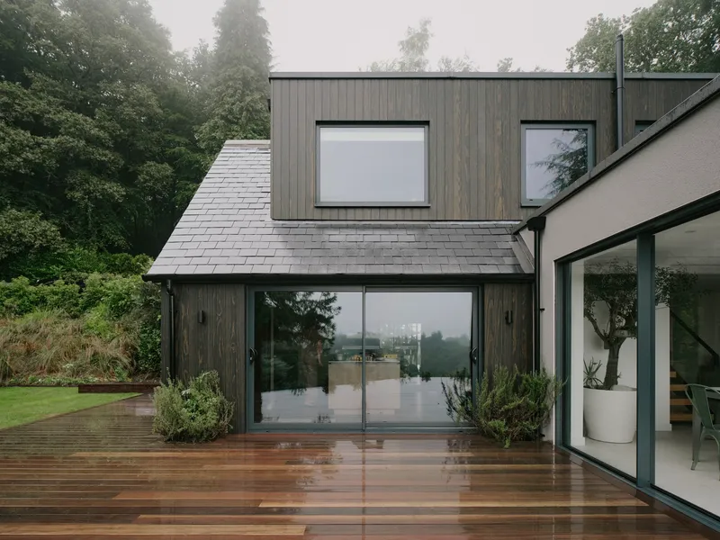 Gable volume with slate roof and timber cladding opening onto rain-soaked timber decking