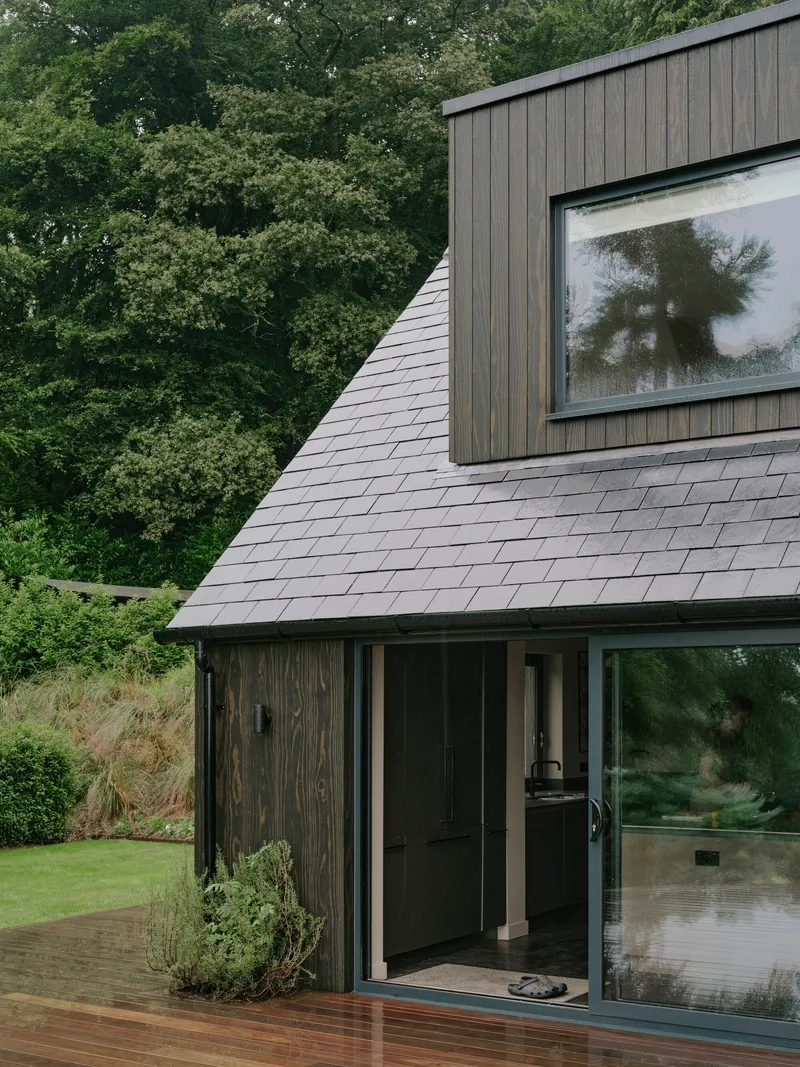 Timber-clad gable with slate roof and corner glazing opening to timber deck and lawn