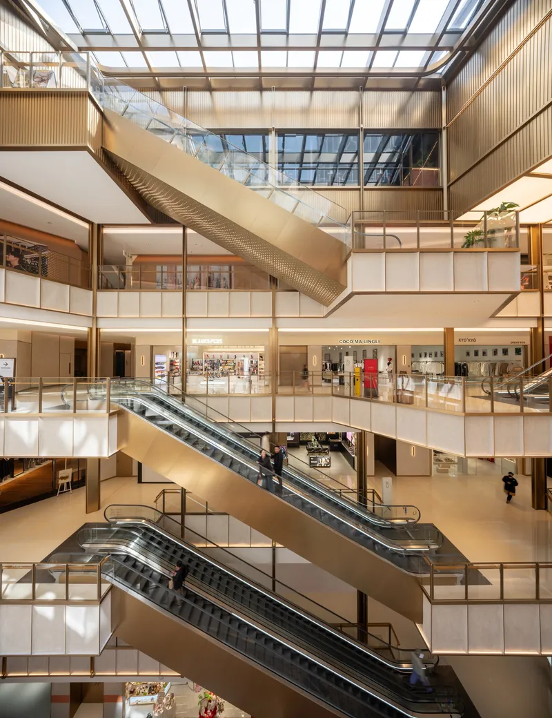 Multi-level atrium interior with escalators connecting floors beneath glazed roof and timber-clad balconies