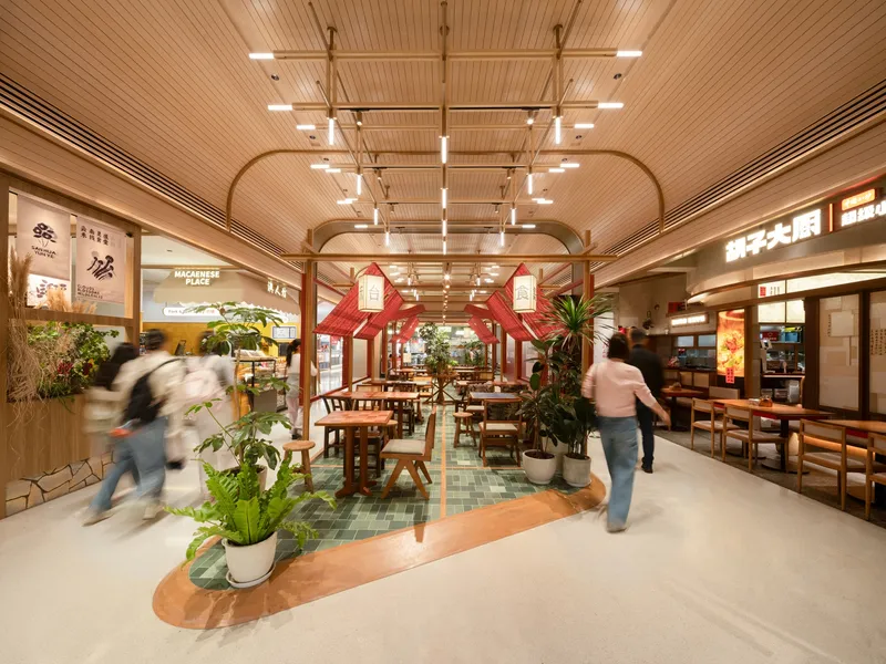 Food court with timber slat ceiling, red kiosk structures, and potted plants as diners move between tables