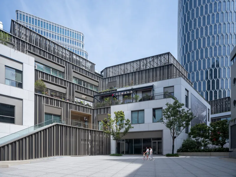 Courtyard plaza with vertical metal fin screens on terraced volumes and two figures crossing the pavement