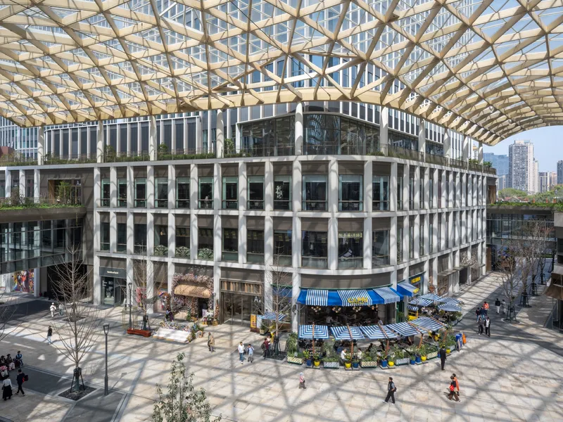 Curved concrete facade with vertical louvers and planted terraces beneath a glass and steel lattice roof