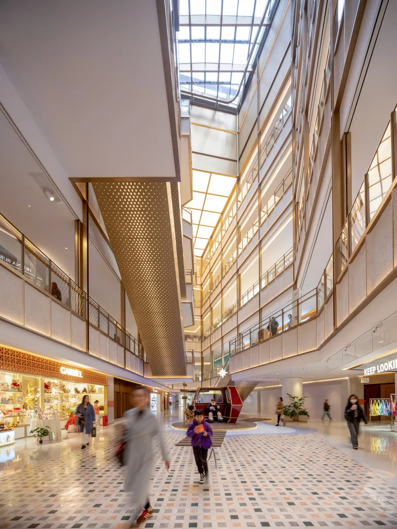 Multi-story atrium with perforated brass column and mosaic floor as shoppers move through daylight below skylights