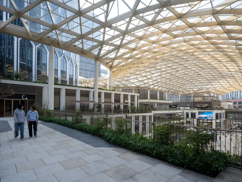 Covered plaza with triangulated timber lattice roof sheltering planted beds and pedestrian walkway below