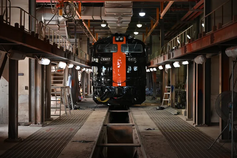 Steam locomotive centered in a maintenance shed with overhead cranes and metal walkways on both sides