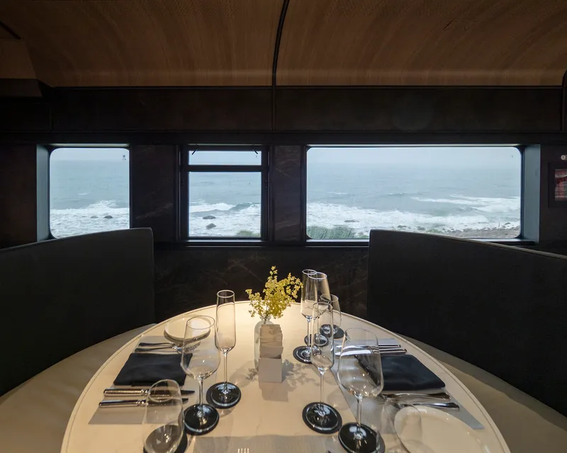 Set dining table with ocean view through train carriage windows framed in dark paneling