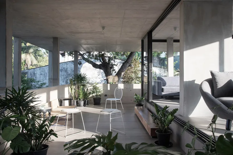 Open concrete terrace with sliding glass doors, white wire chairs and potted plants in morning sunlight