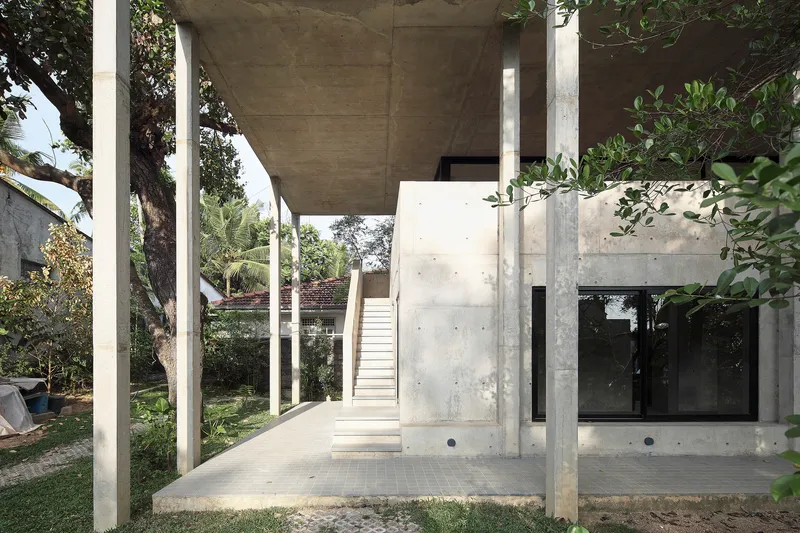 Exterior concrete stair ascending between cylindrical columns beneath the cantilevered upper floor slab