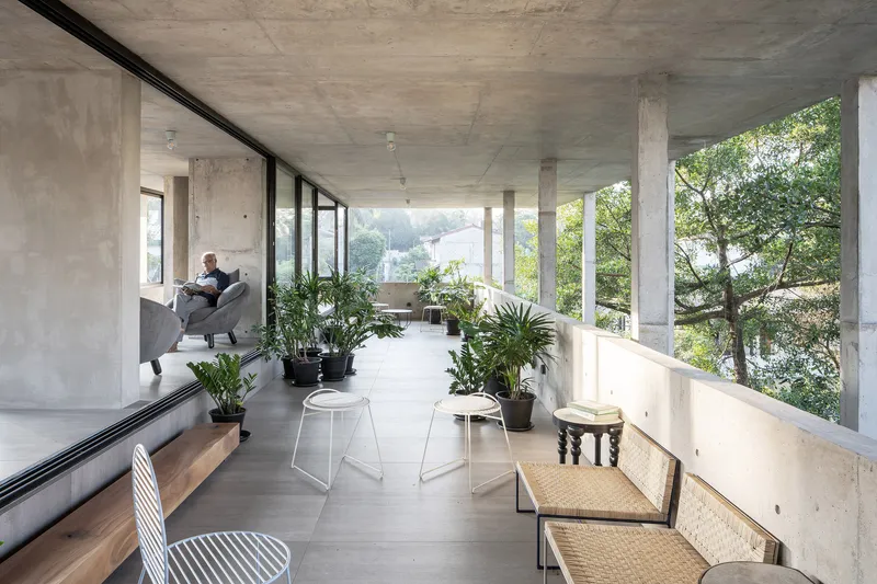 Concrete terrace with exposed ceiling, sliding glass wall, cane bench and person seated in armchair