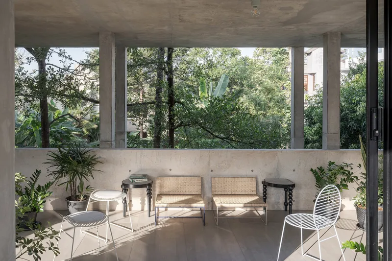 Open-air terrace with cane chairs and potted plants framed by concrete columns overlooking dense foliage