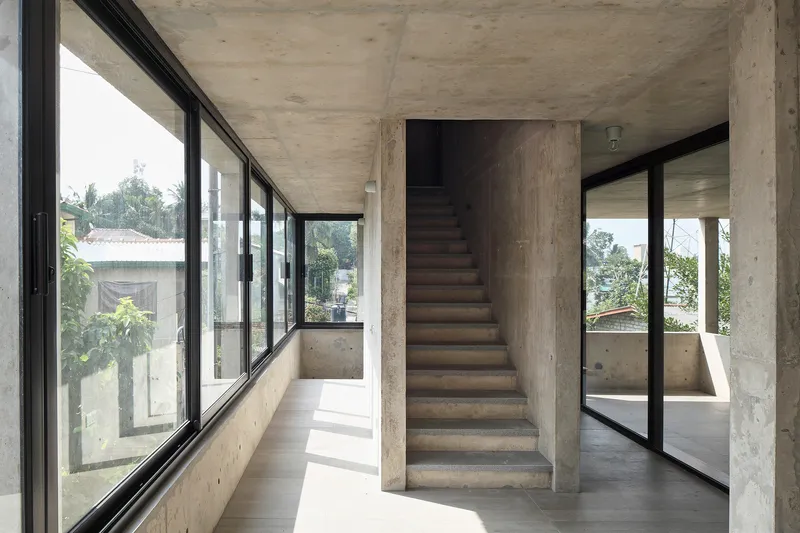 Freestanding concrete staircase flanked by floor-to-ceiling glazing in a sunlit interior