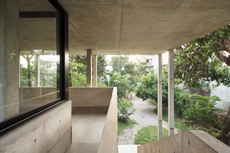 Covered balcony with concrete parapet overlooking a garden path and mature trees at dusk