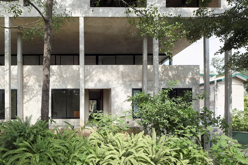 Two-story concrete facade with exposed columns and lush tropical planting in the foreground