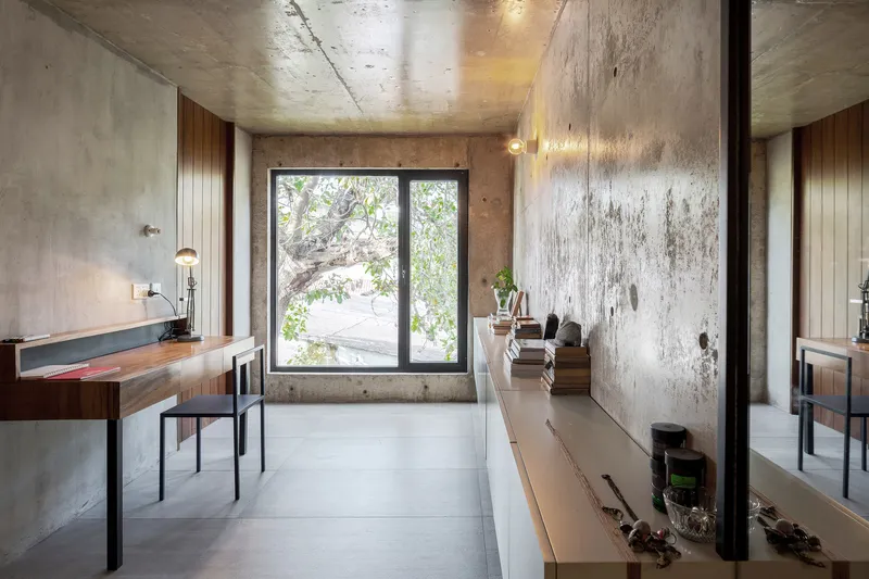 Interior workspace with timber desk, exposed concrete walls and window framing garden views