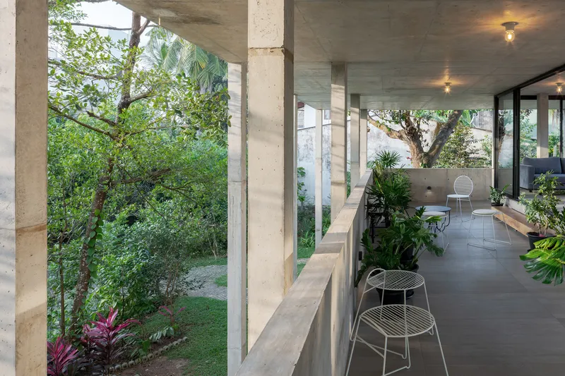 Covered terrace with exposed concrete ceiling and wire chairs opening onto a garden with tropical plants