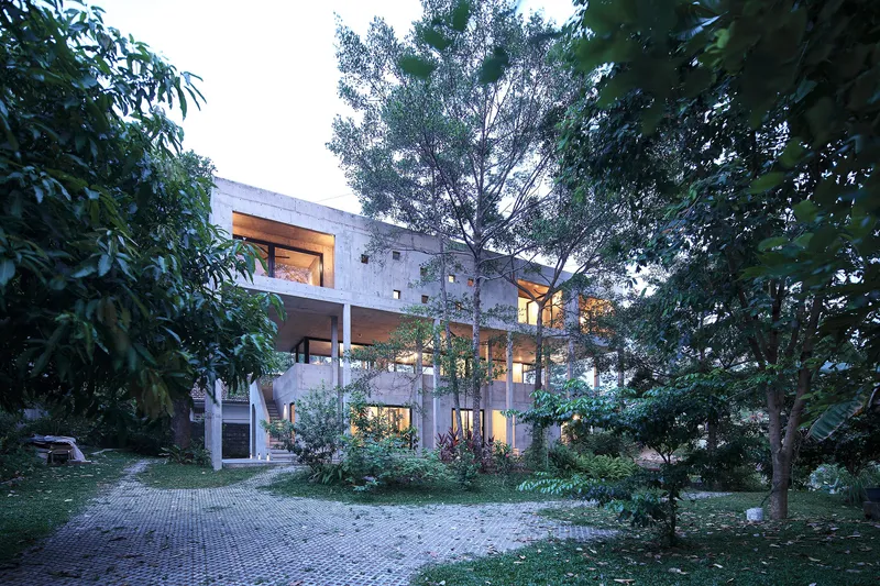 Garden view of the concrete house with recessed balconies amid mature trees at dusk