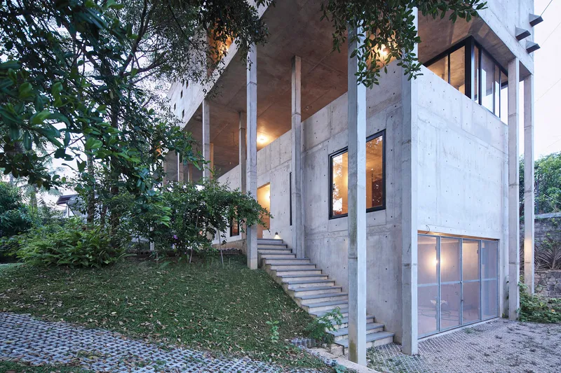 Exterior showing slender concrete columns framing the facade and staircase rising through landscaped slope at twilight