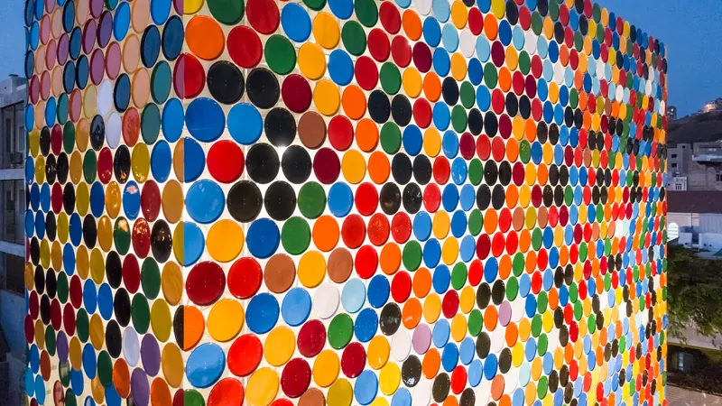 Facade clad in multicolored circular ceramic plates arranged in a honeycomb pattern at dusk