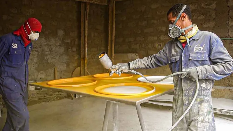 Worker spray-painting yellow finish onto panel with circular cutouts in a construction workshop