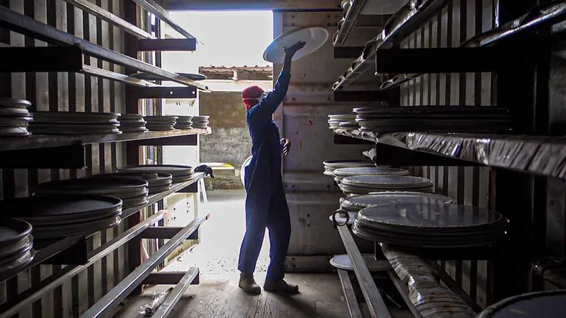 Worker lifting a circular panel component between storage racks in a fabrication facility
