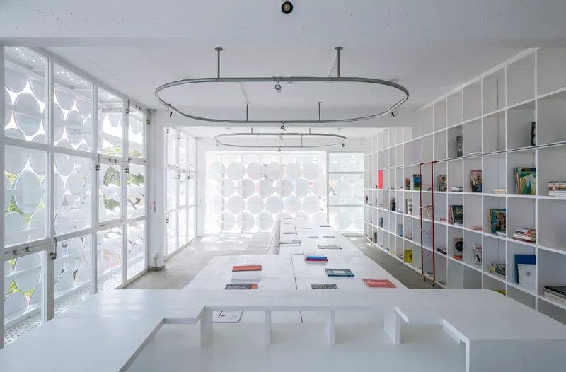 Interior reading room with white shelving, concrete floor, oval ceiling rails and daylight through perforated screens