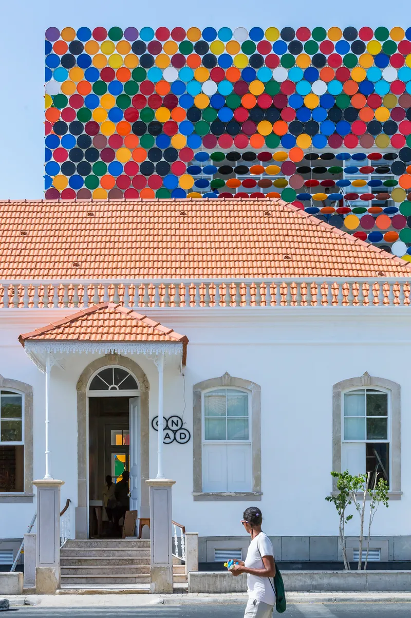 Front elevation of the white building with terracotta roof and colourful disc backdrop at twilight