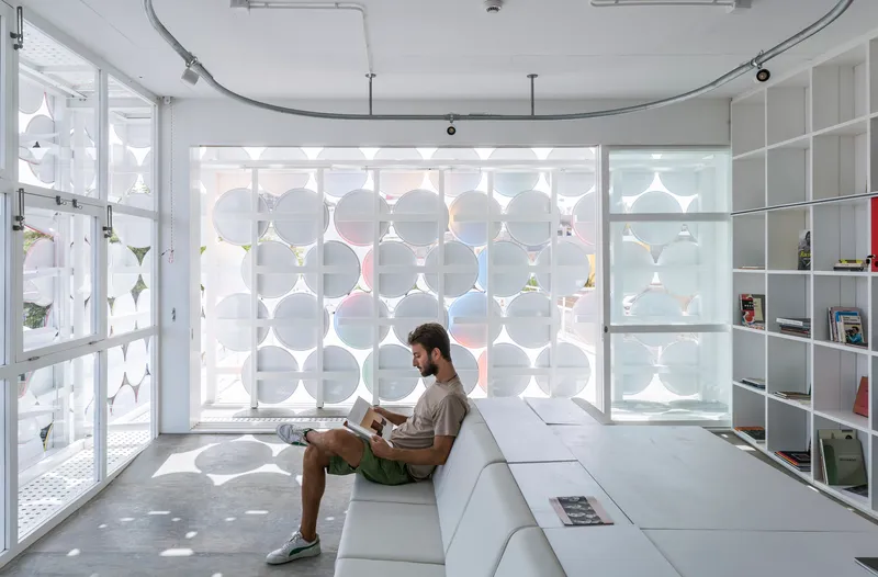 Interior room with circular patterned screen wall casting dappled shadows on a person seated on white platform