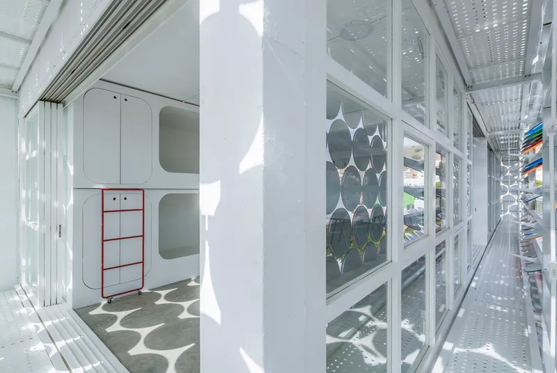 Narrow corridor with perforated metal ceiling and glazed wall overlooking the circular screen facade and plants